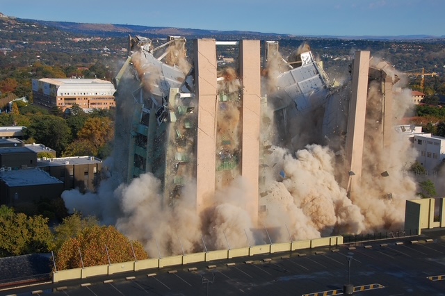 Professional building demolition with hydraulic shear in urban setting